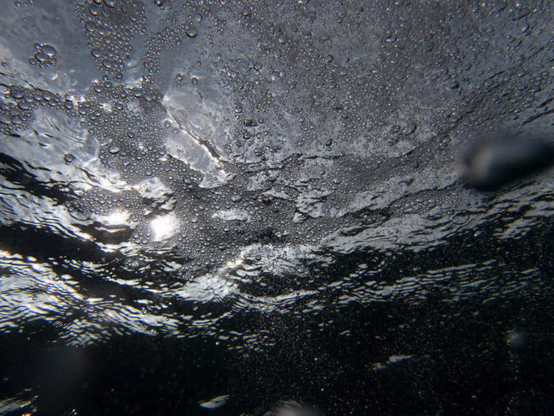 Underwater rising bubbles glimmering with microbubbles and pale light